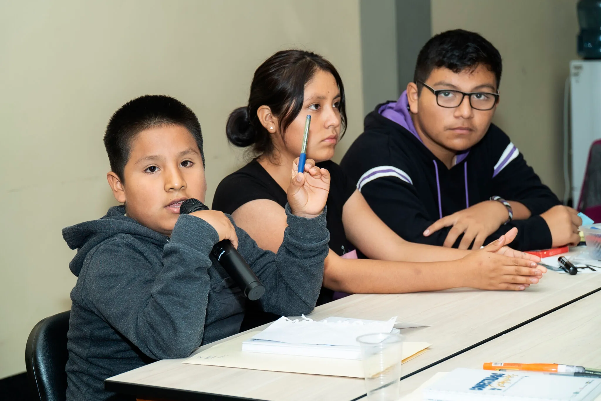 Un niño habla ante un micrófono, acompañado de otras y otros adolescentes.
