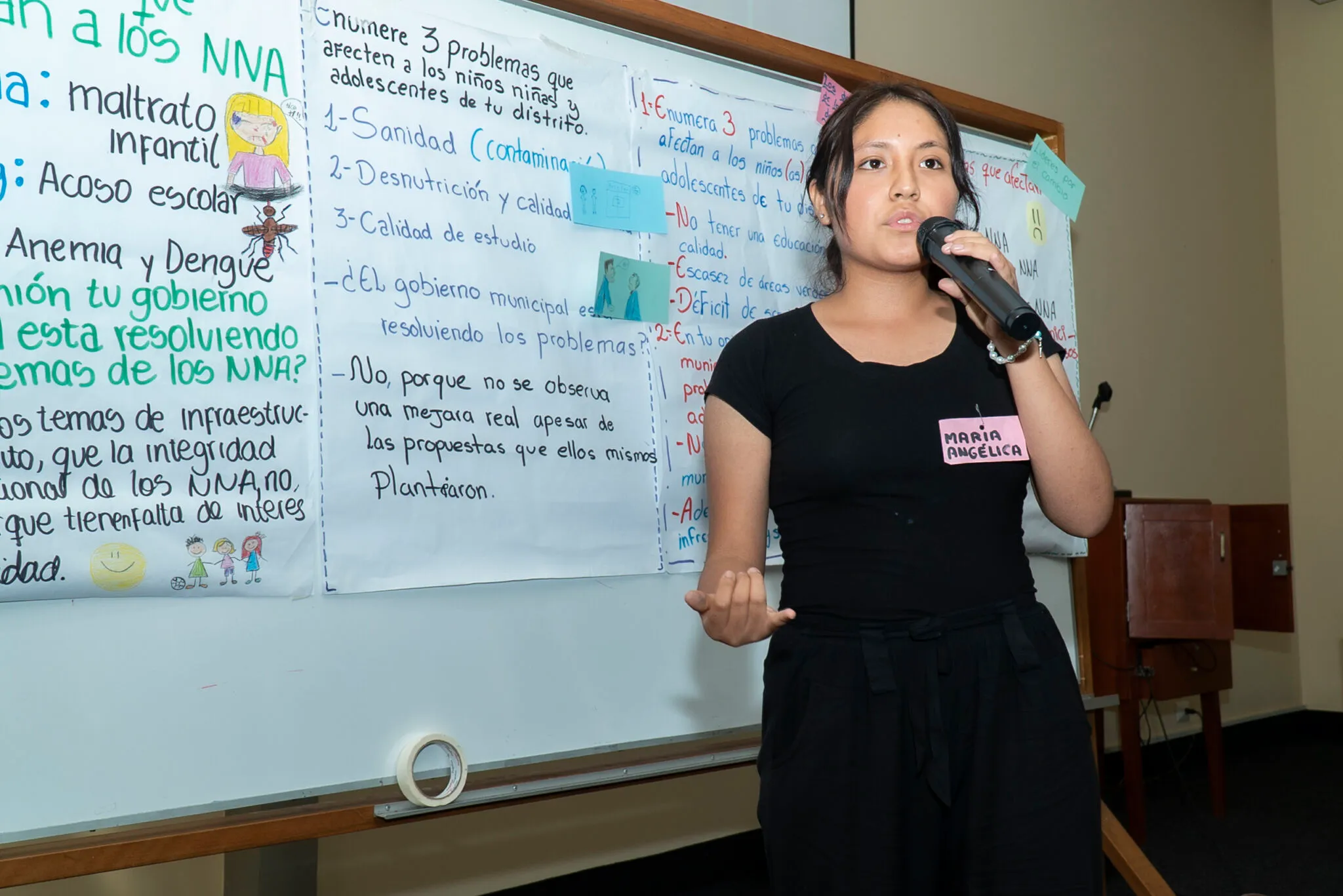 Una adolescente expone ante un micrófono junto a papelógrafos con el análisis del grupo.
