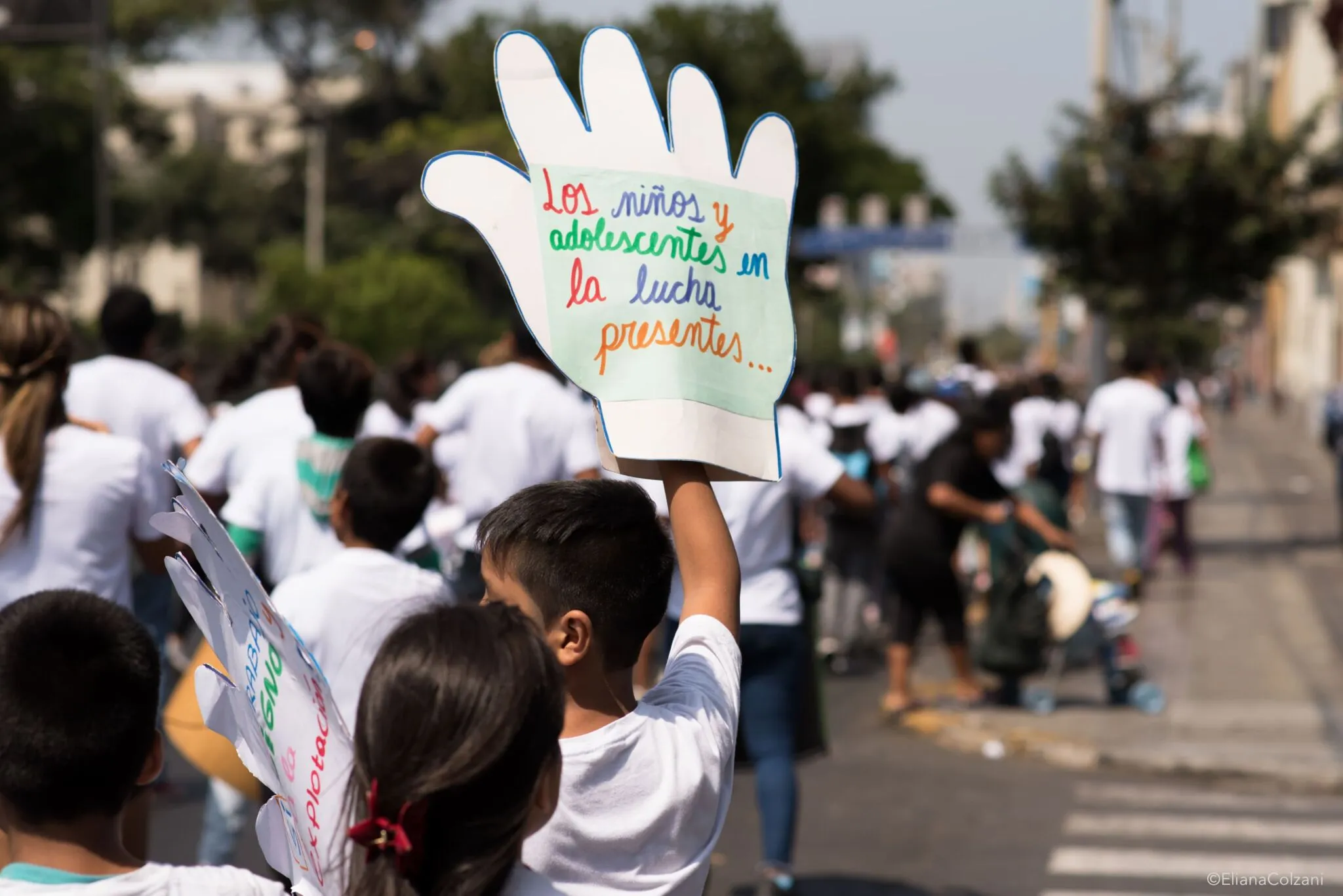 Un niño levanta un cartel en forma de mano que dice «Los niños y adolescentes en la lucha, presentes» durante una marcha.