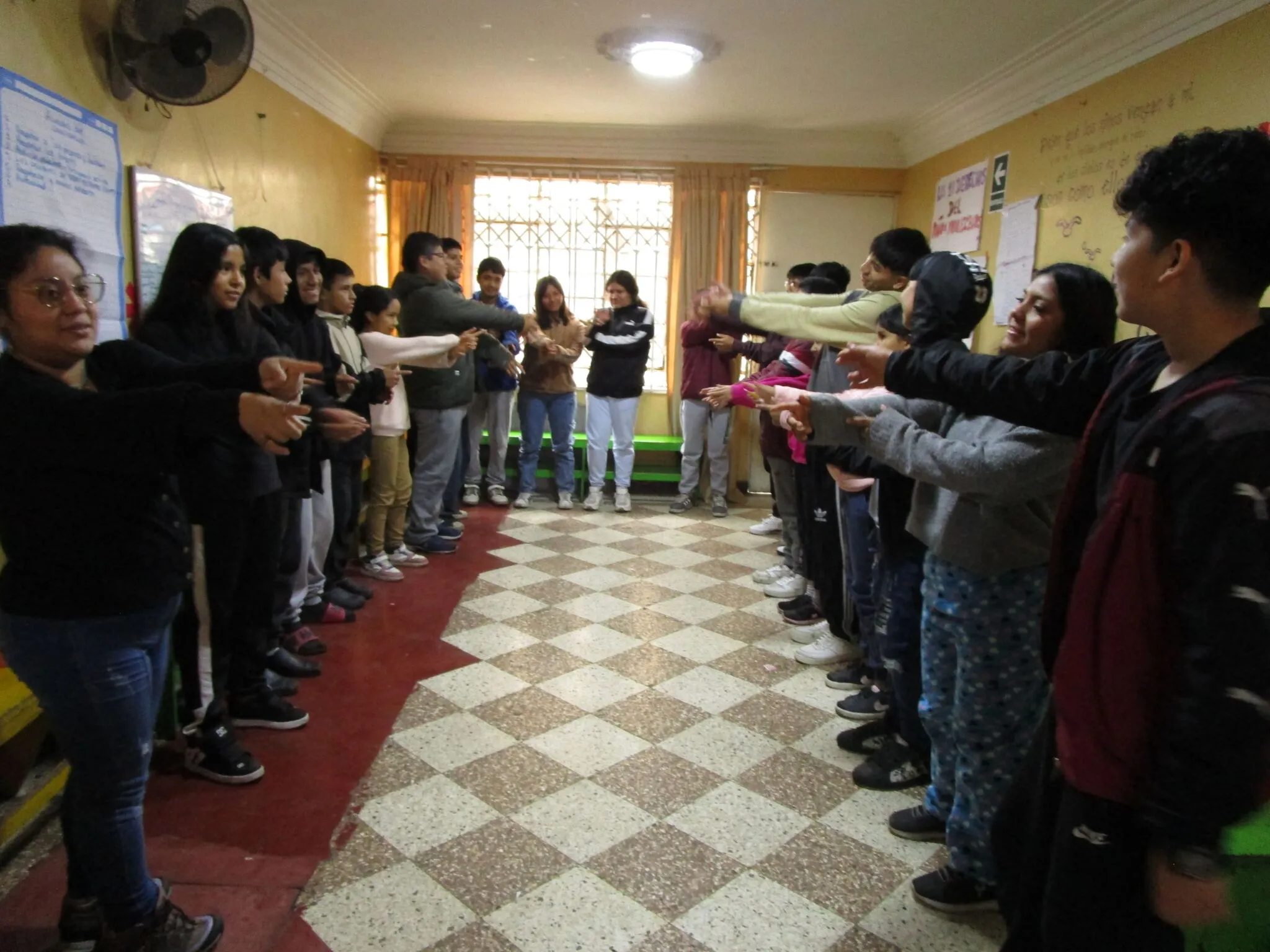 Adolescentes participan de una dinámica en dos filas enfrentadas dentro de un salón.