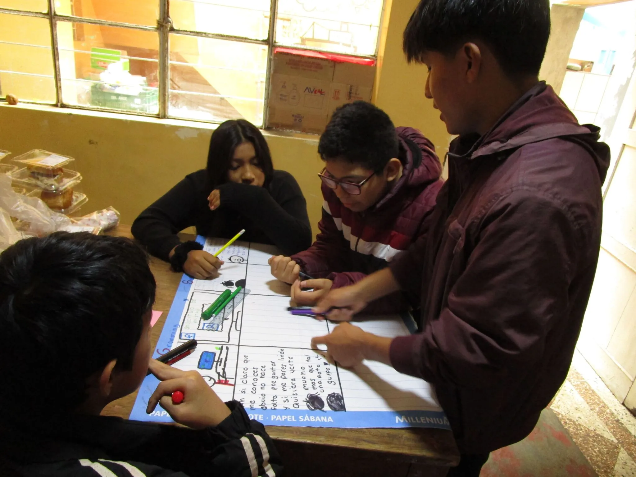 Cuatro adolescentes dibujan y escriben sobre un papelógrafo durante un taller.