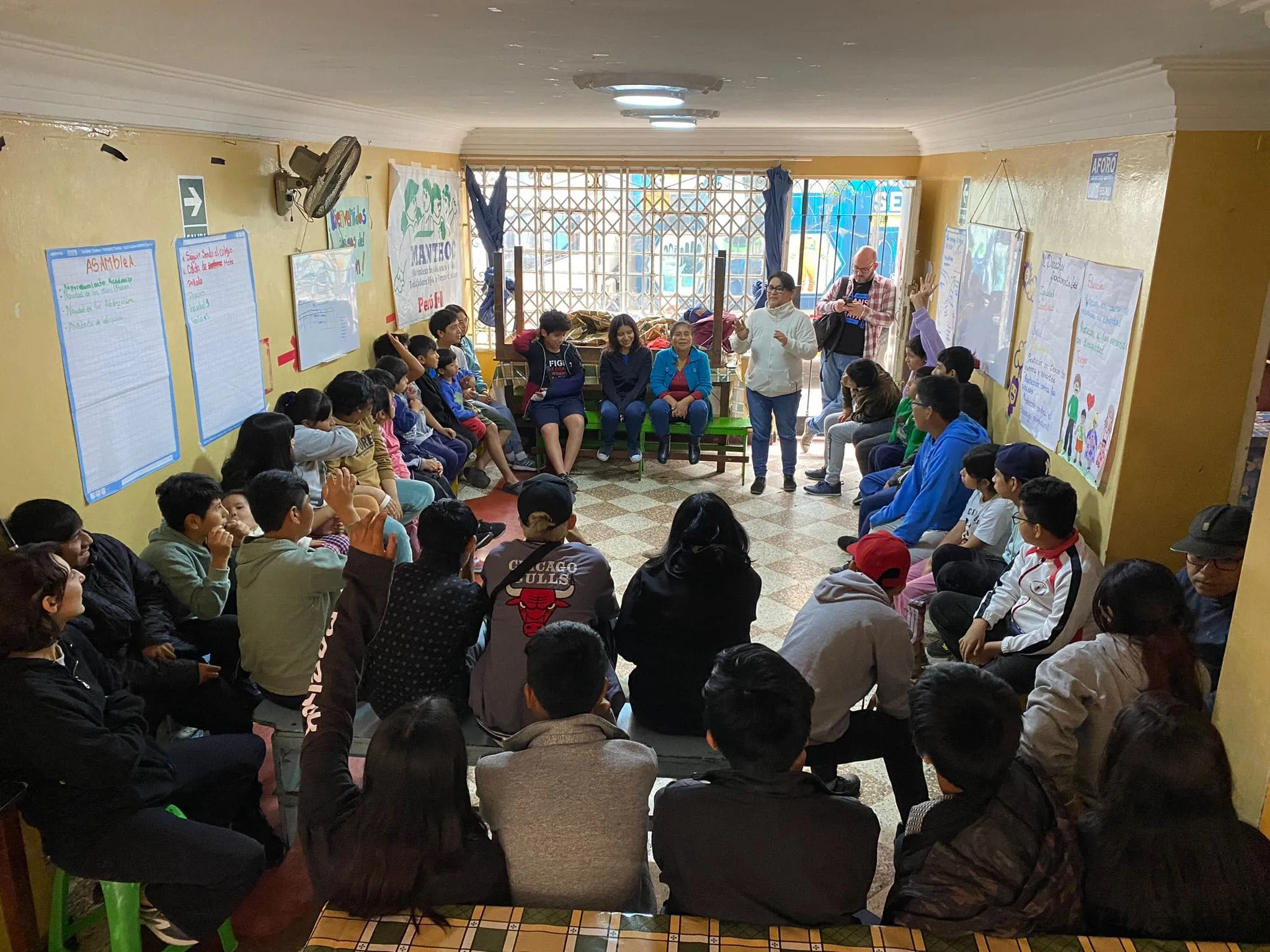 Un grupo de niñas, niños y adolescentes participa en un taller sentado en círculo, con papelógrafos en las paredes.