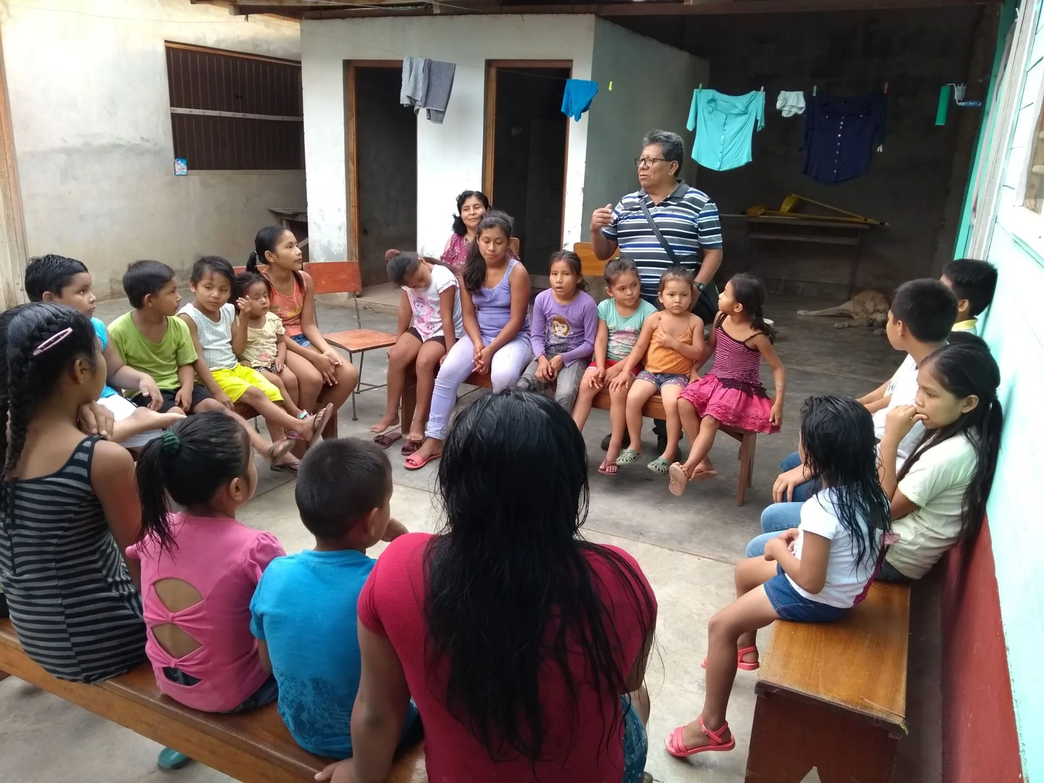 Niñas, niños y adultos conversan sentados en círculo en el patio de una vivienda.