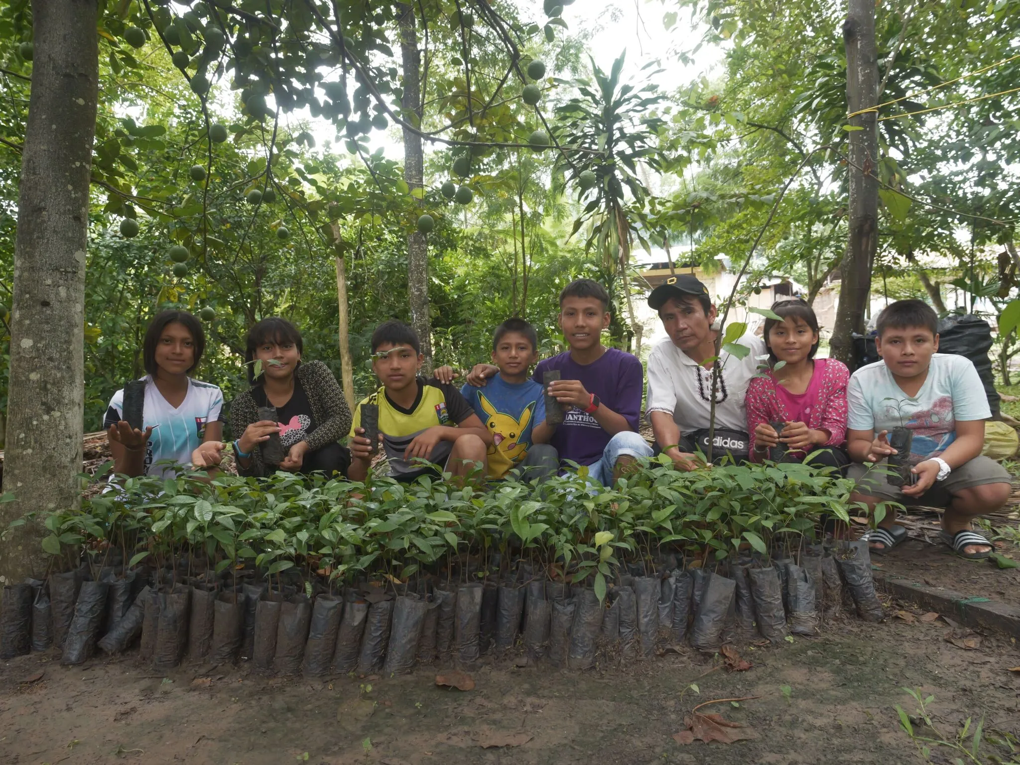 Niñas, niños y adolescentes posan con plantones durante una actividad de reforestación.