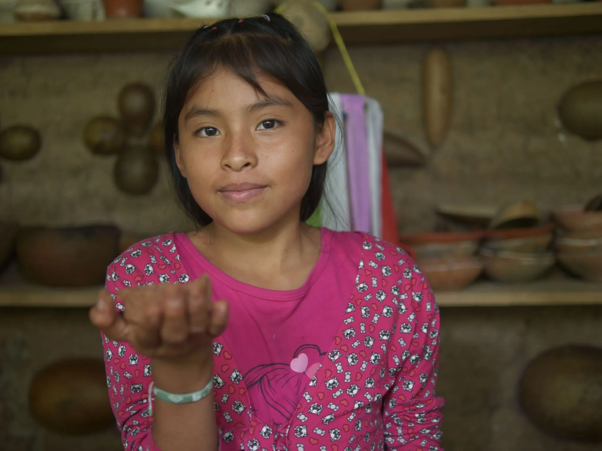 Retrato de una niña que extiende la mano, en un taller de cerámica tradicional.
