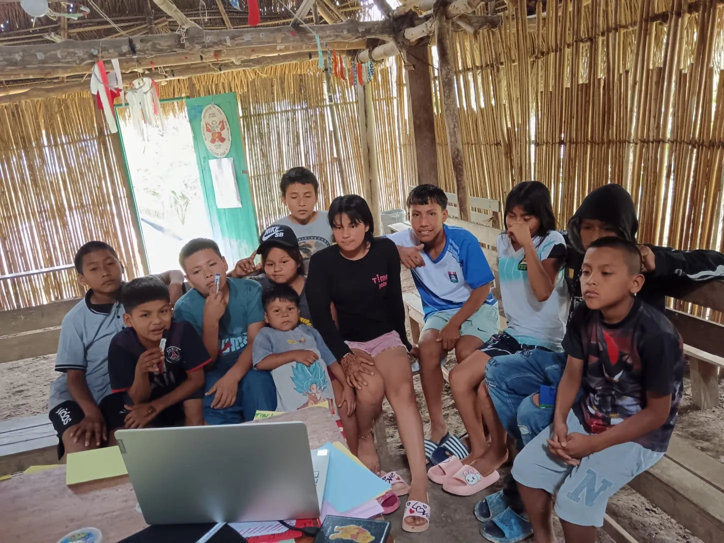Un grupo de niñas y niños se reúne alrededor de una laptop en una vivienda de la Amazonía.