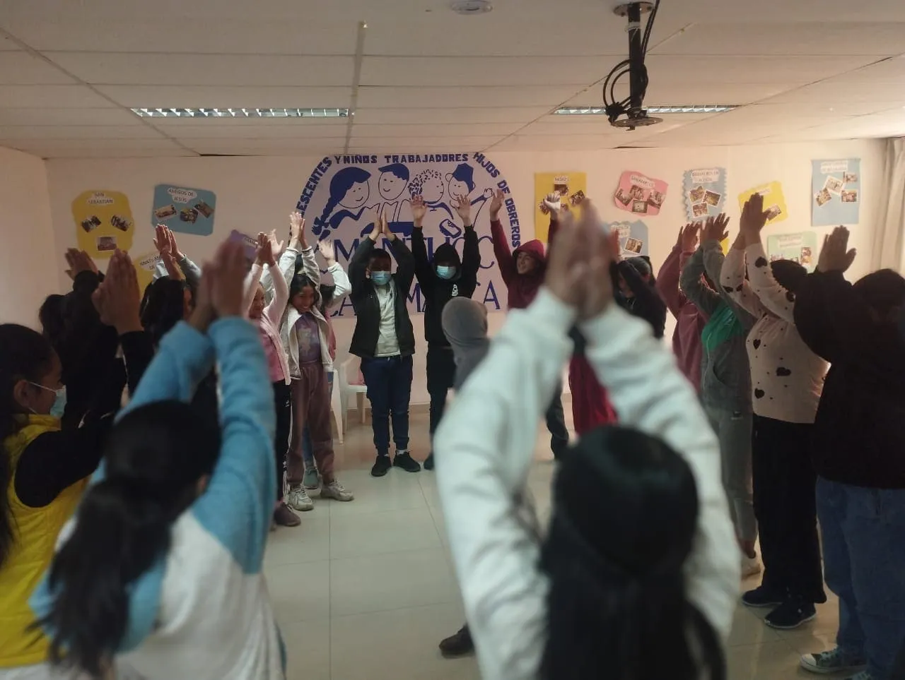 Niñas, niños y adolescentes participan de una dinámica con los brazos en alto en un local de MANTHOC.