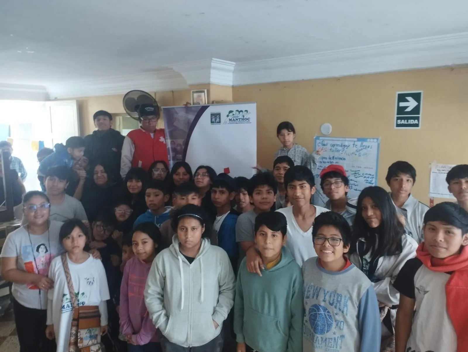 Foto grupal de niñas, niños y adolescentes al final de un taller, junto a un banner de MANTHOC.